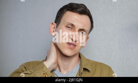 Tired young man suffering neck pain while standing on gray background Stock Photo