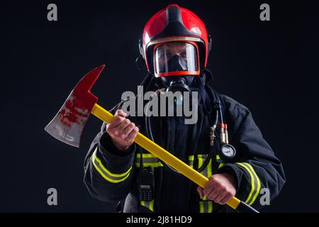 portrait strong fireman in fireproof uniform holding an ax in his hands black background studio Stock Photo