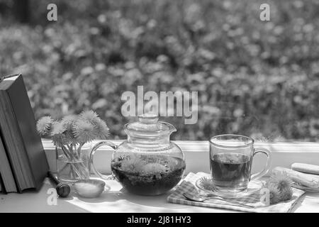 Delicious herbal tea from fresh dandelion flowers with honey on the windowsill at home at summer day near garden, close up, black and white. Hot dande Stock Photo