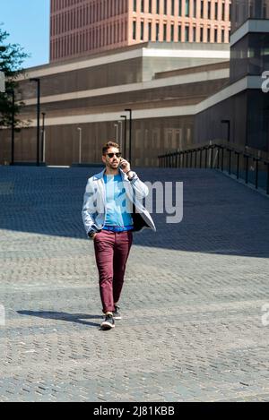 Young bearded man walking in the street while talking by mobile phone Stock Photo
