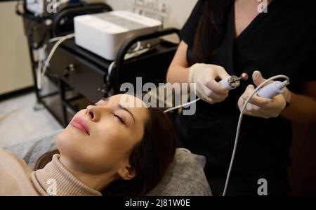 Beautiful young Hispanic woman at spa ready for getting professional cosmetological skin care and anti-aging treatment with electrical impulses on her Stock Photo
