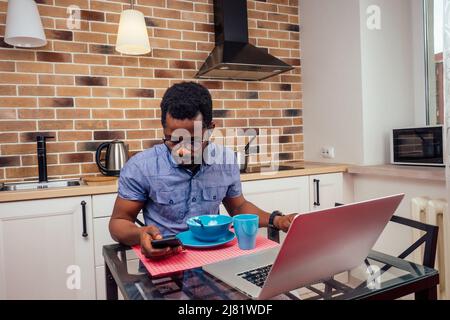 african - american male overworkind laptop night work alone at kitchen,brick wall with lamps and cooker hood background Stock Photo