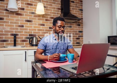 african - american male overworkind laptop night work alone at kitchen,brick wall with lamps and cooker hood background Stock Photo