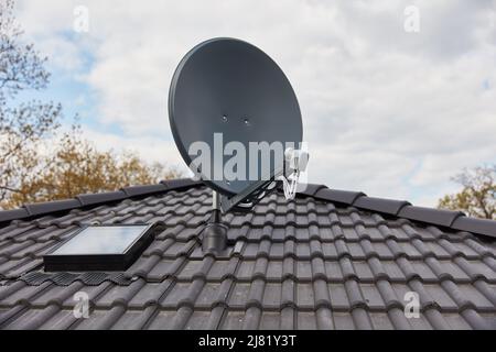 Satellite dish on the roof of the house next to the skylight for maintenance and care of the satellite system Stock Photo