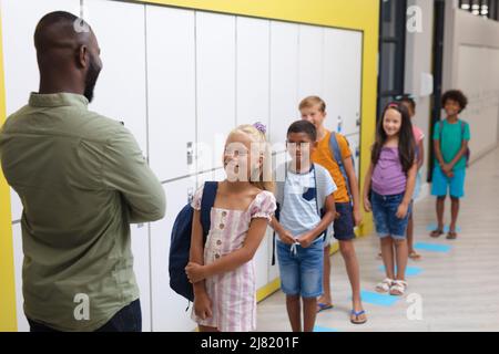 African american young male teacher looking at multiracial elementary students standing in row Stock Photo