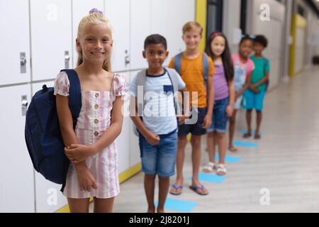 Portrait of smiling multiracial elementary school students standing in row by lockers in corridor Stock Photo