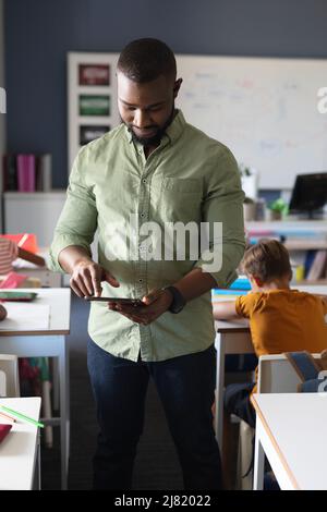 African american young male teacher using digital tablet while standing in classroom Stock Photo