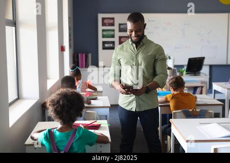 African american young male teacher using digital tablet while standing by multiracial students Stock Photo