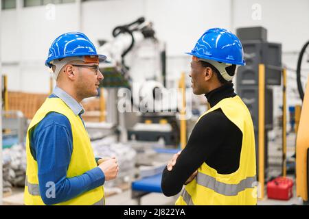 Multiethnic engineers working inside robotic factory - Industrial and technology concept - Focus on left man hat Stock Photo