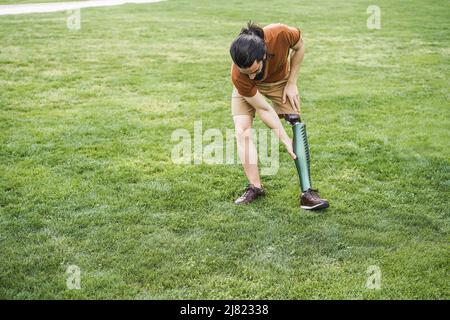Young man adjusting his prosthetic leg outdoor - Focus on hand holding prosthesis Stock Photo