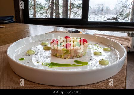 The salad of various ingredients is beautifully arranged in the form of a ring on a white plate. Stock Photo