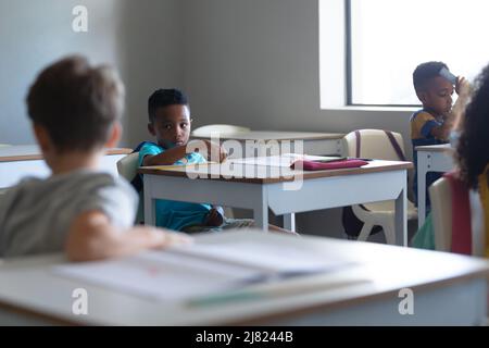 Multiracial elementary school students sitting at desk in classroom Stock Photo