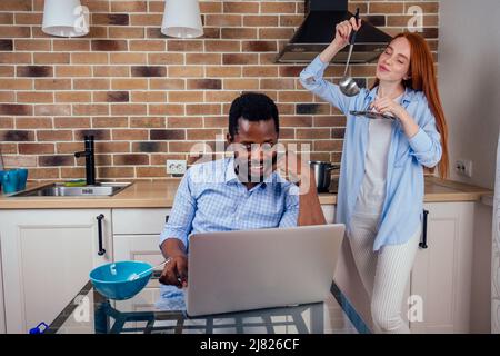 caucasian redhaired ginger woman cooking traditional russian soup borscht to her african-american man in kitchen Stock Photo