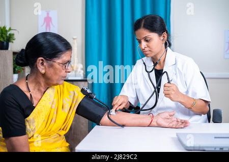 Doctor checking blood pressure or bp of senior woman patient at hospital - concept of health care, medical treatment and consultation. Stock Photo