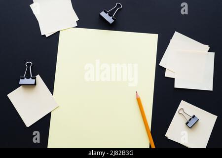 top view of blank paper near sticky notes and fold back clips on black Stock Photo