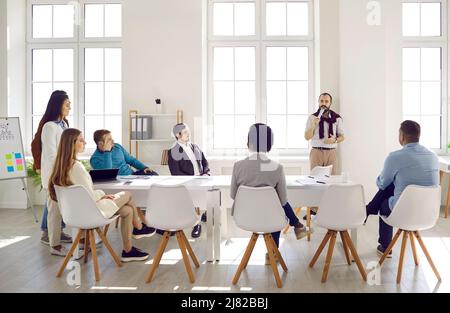 Diverse team of people listening to business coach during meeting in modern office Stock Photo