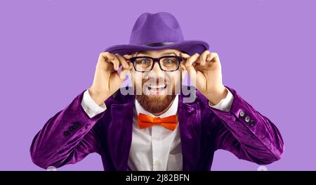 Portrait of funny cheerful stylish showman who wears glasses while standing on purple background. Stock Photo