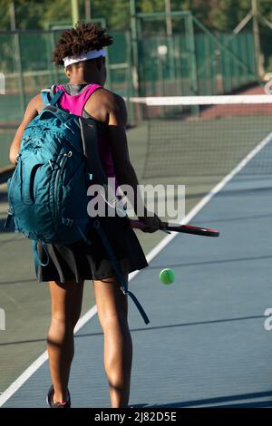 Rear view of african american young female tennis player with backpack walking at court on sunny day Stock Photo