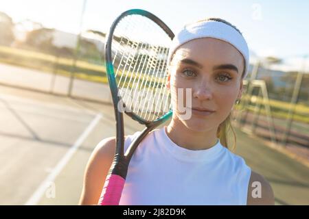 Portrait of beautiful young female caucasian tennis player wearing headband holding racket court Stock Photo