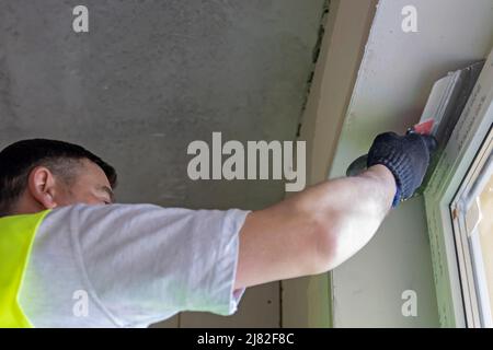 The master levels the wall with a spatula, applying the plaster mixture on the wall. Stock Photo