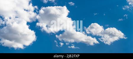 Sunlit white clouds on blue sky in abstract panoramic cloudscape background. Scenic panorama with beautiful group of fluffy cloud cumuli in hot summer. Stock Photo