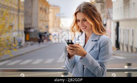 Smiling blonde young girl business woman looking at mobile phone winning rejoices victory triumph makes yes hand gesture shopping online happy with Stock Photo