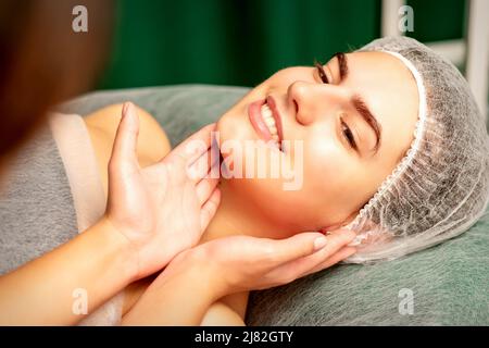 Plastic surgery and beauty concept. Professional cosmetician examining and touching the face of the beautiful young caucasian smiling woman in a clinic of esthetic cosmetology Stock Photo