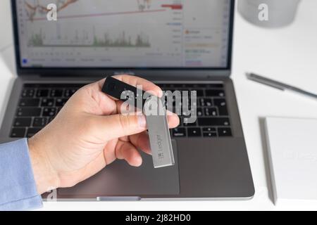 Russia, Krasnodar - April 15, 2022: Hand holding hardware cryptocurrency wallet Ledger on laptop background. Safe storage for crypto. closeup Stock Photo