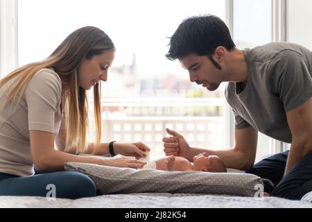 a couple of parents changing the diapers to their newborn son on the bed Stock Photo