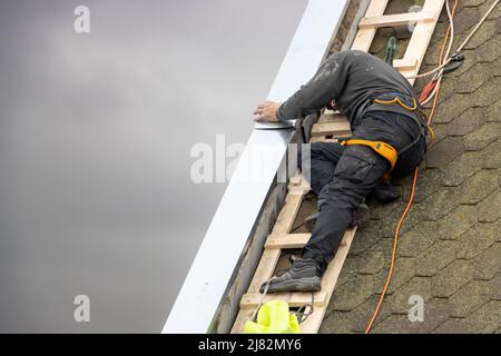 A man works on the roof repair, installs sheet metal on top of the gable wall Stock Photo