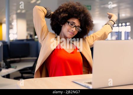 Tired young female african american advisor stretching while looking at laptop in workplace Stock Photo