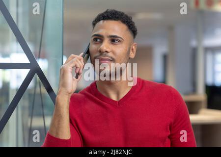 Thoughtful young hispanic businessman looking away while talking on smartphone Stock Photo