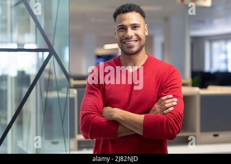 Portrait of happy hispanic male advisor standing with arms crossed at modern workplace Stock Photo
