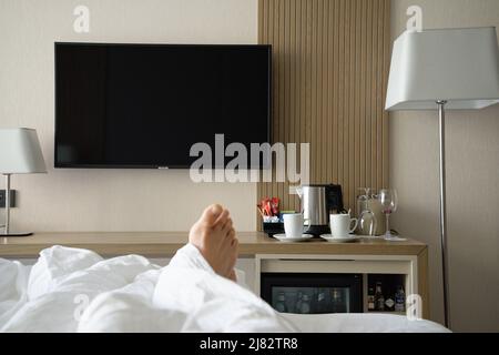 In bed in a nondescript hotel room with tea and coffee making facilities, a TV and a minibar fridge. Stock Photo