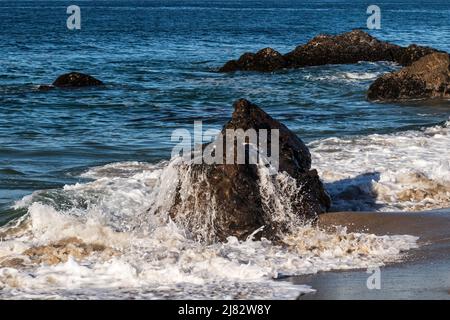 Water draining from a rock exposed at low tide, at the beach near Malibu, California. Blue Pacific Ocean in the background. Stock Photo