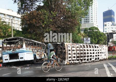 Colombo, Sri Lanka. 12th May, 2022. A man rides past buses destroyed in the clashes few days ago during a few hours' relaxation of the ongoing curfew in Colombo, Sri Lanka, May 12, 2022. Sri Lanka imposed a nationwide curfew following violent clashes in the capital Colombo on May 9. Credit: Tang Lu/Xinhua/Alamy Live News Stock Photo