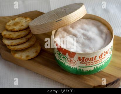 Vacherin cheese in round wooden box served on a wooden board with crackers. Stock Photo