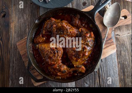 Braised chicken legs with a spicy tomato sauce. Served in a cast iron skillet isolated on wooden table. Top view with copy space Stock Photo