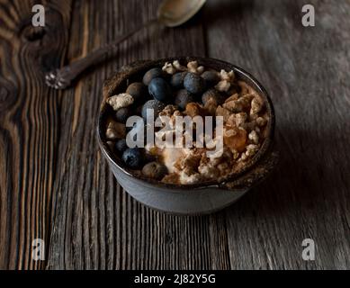 Breakfast bowl with yogurt, puffed brown rice, blueberries, pumpkin and cinnamon. Isolated on wooden table with copy space Stock Photo