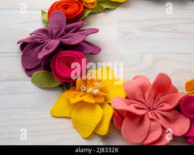 Close-up of colourful handmade felt flower garland on lime-washed wooden background. Stock Photo