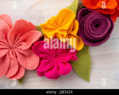 Close-up of colourful handmade felt flower garland on lime-washed wooden background. Stock Photo