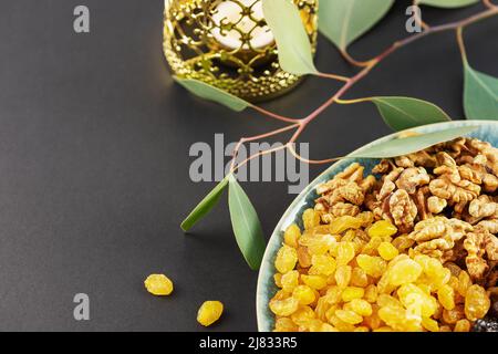 Ramadan concept. Nuts, dried fruits and dates in the blue bowl, ramadan lantern and green branch on a black background with copy space. Arab dish, swe Stock Photo