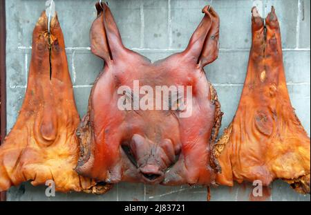 Fenghuang, Hunan Province, China: Meat from a pig's head and legs hanging up for sale at a butchers shop in Fenghuang. Stock Photo