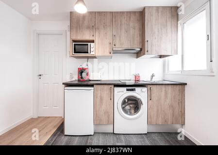 Kitchen with wood-colored cabinets, white appliances, dark countertops, and multi-colored hardwood floors Stock Photo