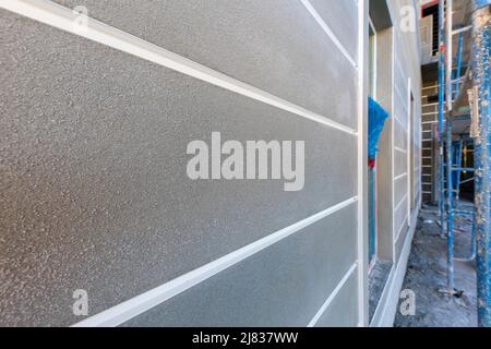 freshly applied stucco to an exterior wall of an apartment building with sprayed on final finish between vinyl corner beading Stock Photo