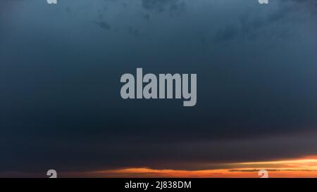 Aerial wide panoramic epic dark cloudscape view above vivid orange sunset layers. Blue heavy clouds covering colorful evening sky scene Stock Photo