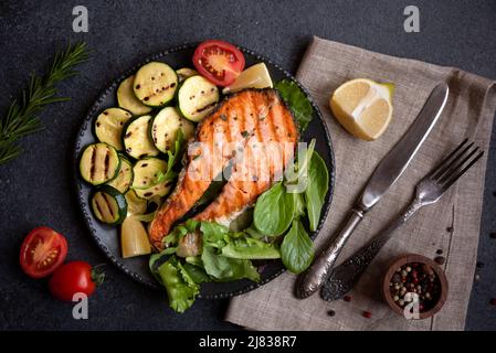 Cooked salmon fish with herbs and vegetables on dark background Stock Photo