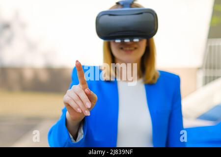 Business woman controls the virtual interface by pressing buttons with her finger in VR goggles in the park Stock Photo