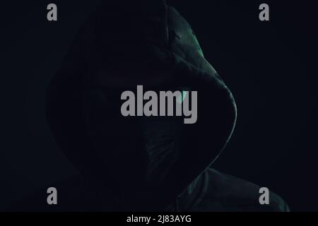 Stylish man dark hoodie, black glasses and mask green background, hacker, attacker and bandit Stock Photo