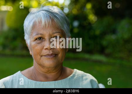Close-up portrait of confident biracial senior woman with short gray hair against plants in park Stock Photo
